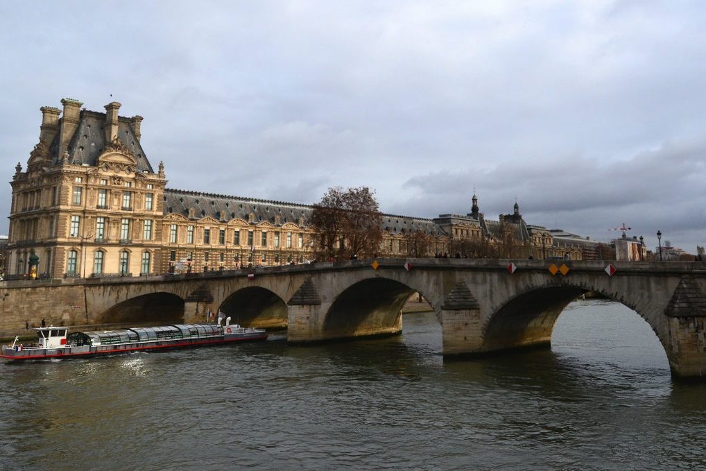Passenger boat emerges from the Pont Royal across the River Seine at the Louvre.